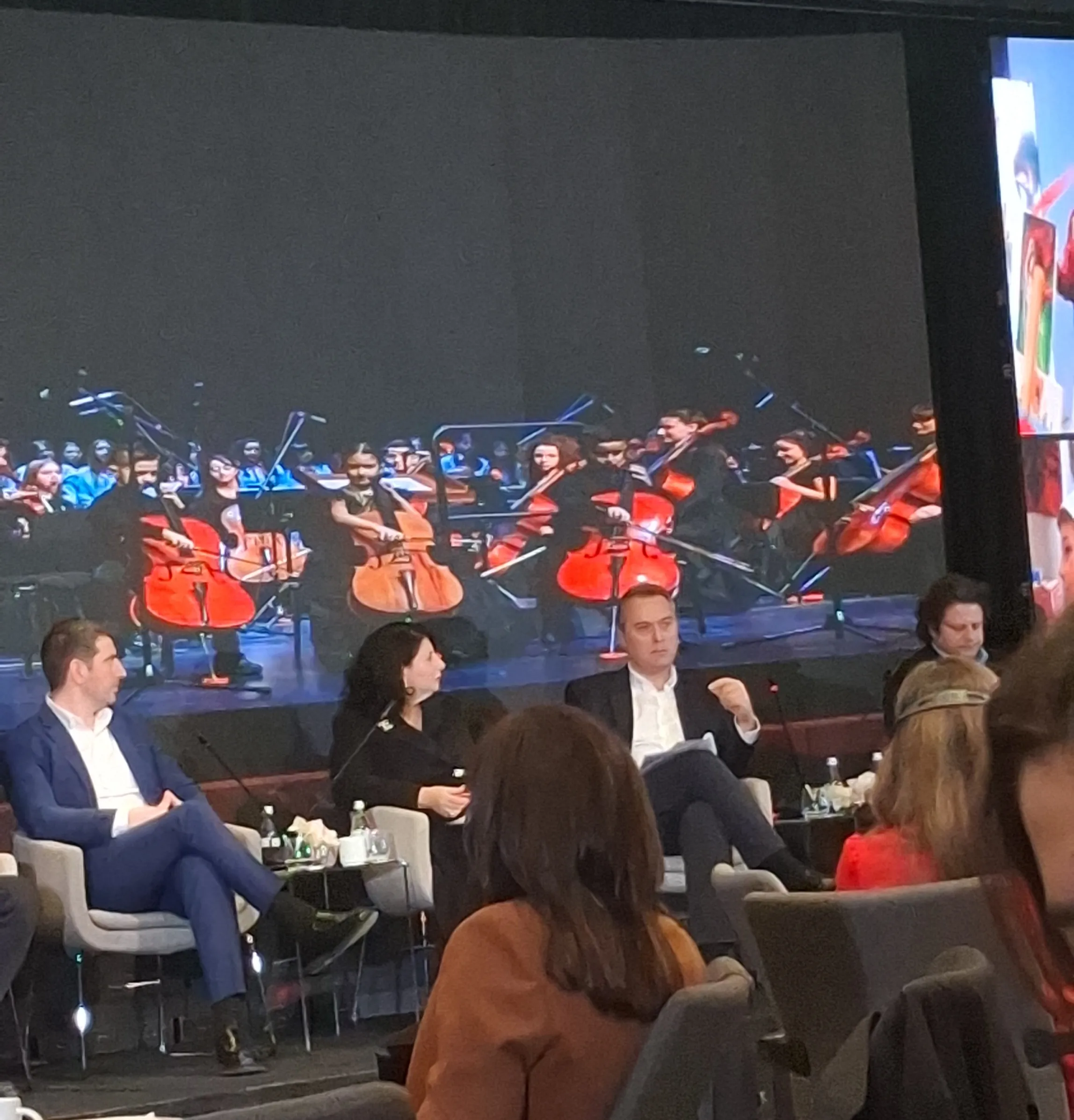 Paneli i konferencës gjatë diskutimit, me publikun në sallë dhe ekranin në sfond
